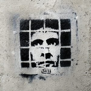 Stencil design of a prisoner painted on a concrete wall, male face framed by a grid of bars